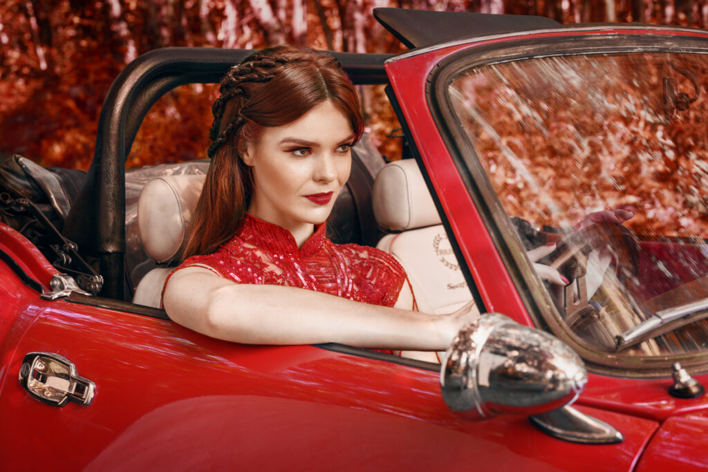 Woman in red dress driving red Triumph Spitfire