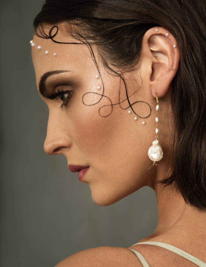 profile view of young woman with dark hair, curls and pearls