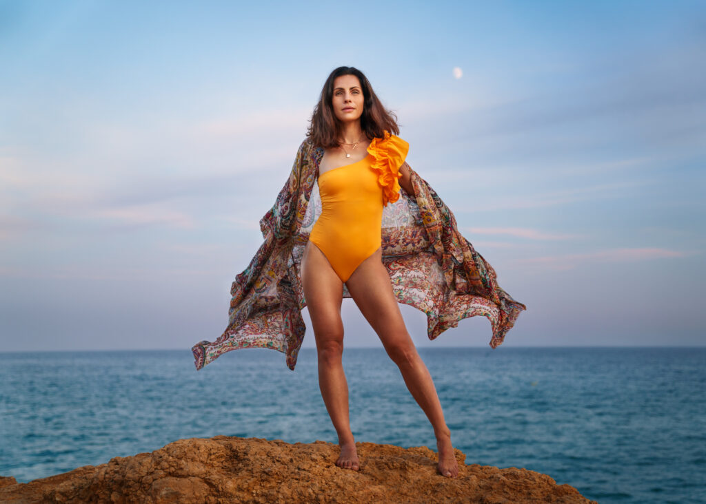 woman in orange up on a rock over the ocean